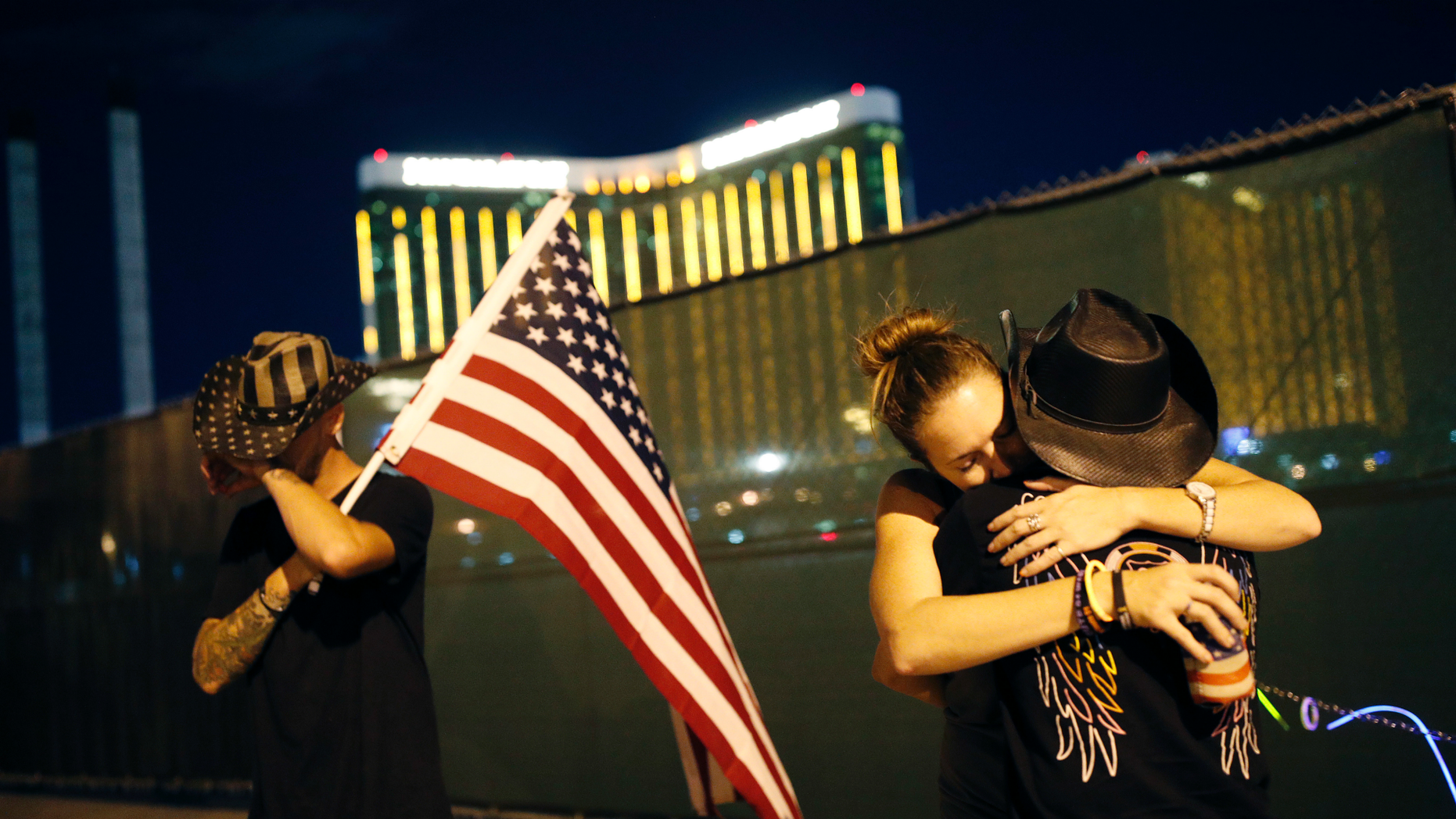 Megan Murphy, while wearing a hat, kisses Cara Knoedler as Kenneth Wright wipes his eyes off the first anniversary of the mass shooting on Monday, October 1, 2018 in Las Vegas. Behind them is the filming site. Hundreds of mass shooting survivors in Las Vegas formed a human chain around the closed site of a country music festival where an armed gunman opened fire on October 1, 2017. (AP Photo / John Locher)