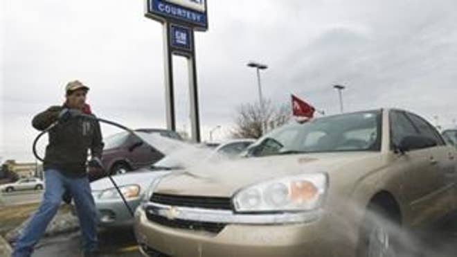 An employee at a General Motors dealership washes down cars (AP Photo).
