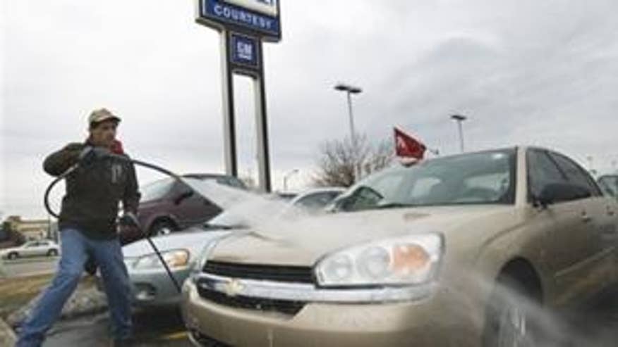 An employee at a General Motors dealership washes down cars (AP Photo).