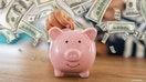 Close up of little boy saving coin into piggy bank at home. Closeup of child hand putting penny coin in piggy bank on table. Kid saving money by adding coin in pig shaped bank.