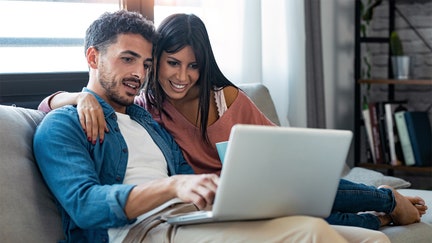 Shot of happy beautiful couple using computer while sitting on the couch at home.