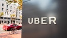 Sign with logo at the headquarters of car-sharing technology company Uber in the South of Market (SoMa) neighborhood of San Francisco, California, with red vehicle visible in the background parked on Market Street, October 13, 2017. SoMa is known for having one of the highest concentrations of technology companies and startups of any region worldwide.