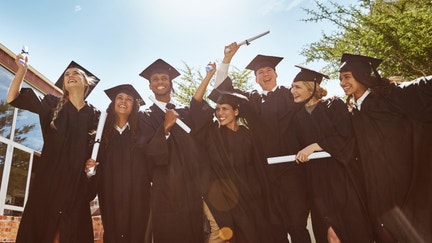 Students smile and wave diplomas after their college graduation.