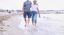 A retired couple walks arm in arm on the beach. 
