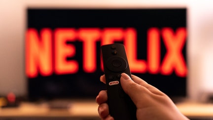 A hand holding a tv remote with a ''Netflix button'' is seen in front of a tv screen with the logo of Netflix. (Photo by Nikos Pekiaridis/NurPhoto via Getty Images)

