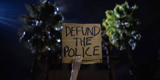 A protester holds up a sign as a police helicopter flies by in front of the South Los Angeles Sheriff's Department during protests following the death of Dijon Kizzee on Monday, Aug. 31, 2020, in Los Angeles. (AP Photo/Christian Monterrosa)