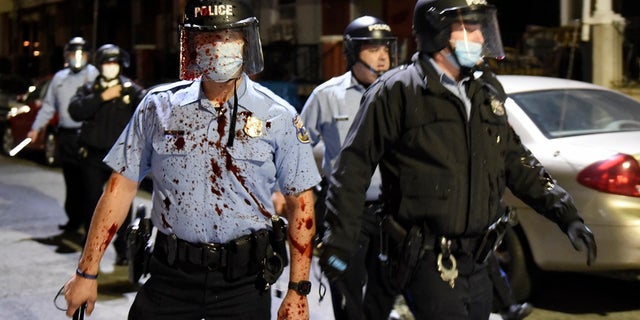 A Philadelphia police officer is covered with an unidentified red substance during a confrontation with protesters, Tuesday, Oct. 27, 2020, in Philadelphia. (AP Photo/Michael Perez)