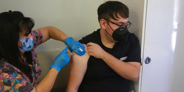 Marcos Enriques Flores, a summer camp kitchen worker and business school student, looks away as a health ministry nurse taking the COVID-19 vaccine at a mobile clinic in the Glorieta Adventure camp. (AP Photo / Cedar Attanasio)