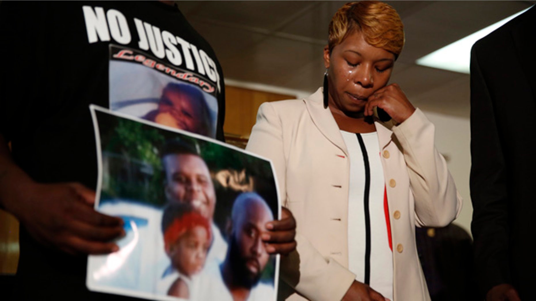 Aug. 11, 2014: Lesley McSpadden, the mother of 18-year-old Michael Brown, wipes away tears as Brown's father, Michael Brown Sr., holds up a family picture of himself, his son, top left, and a young child during a news conference in Jennings, Mo. (AP/Jeff Roberson, File)