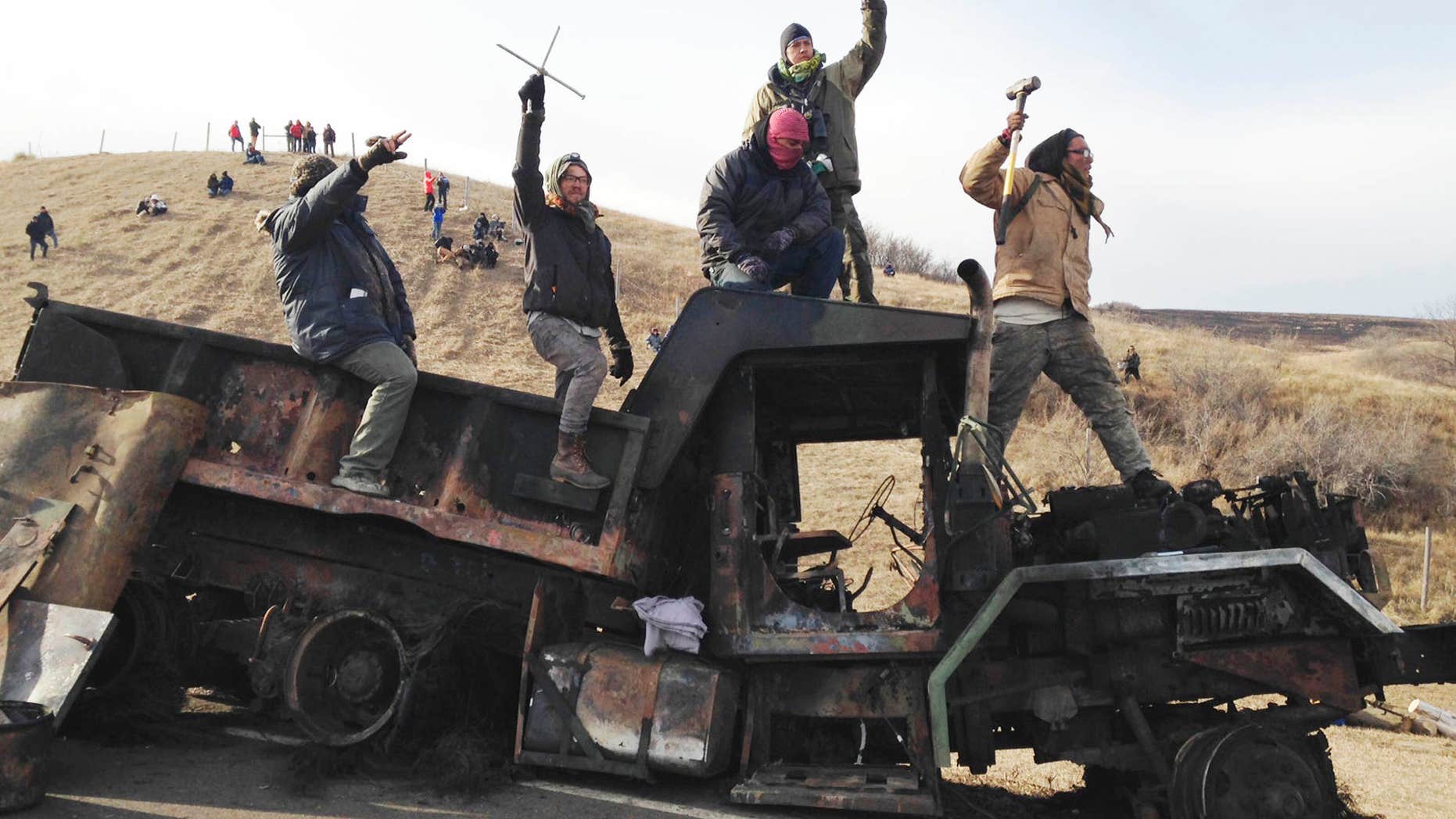 FILE - In this Monday, Nov. 21, 2016, file photo, protesters against the Dakota Access oil pipeline stand on a burned-out truck near Cannon Ball, N.D., that they removed from a long-closed bridge a day earlier on a state highway near their camp.