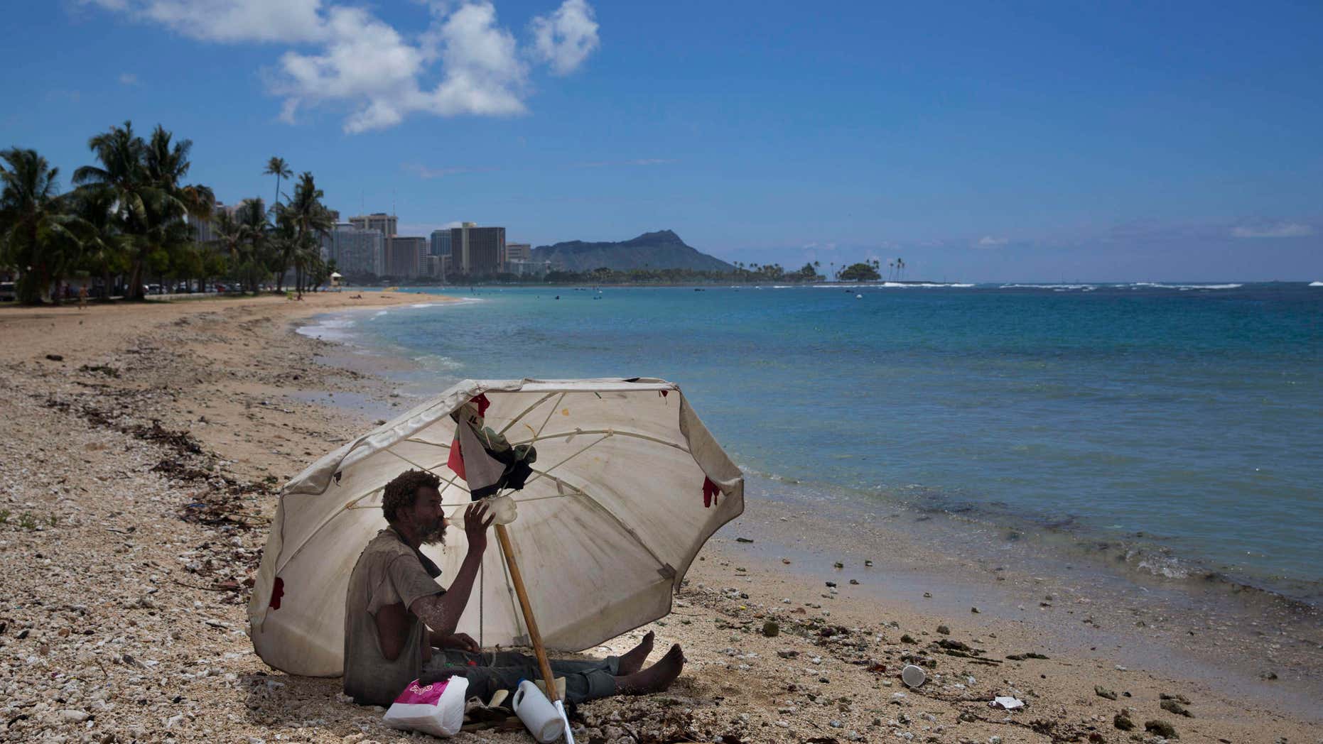 FILE - In this Aug. 27, 2015, file photo, a homeless man drinks water while sitting on the beach at Ala Moana Beach Park located near Waikiki in Honolulu.