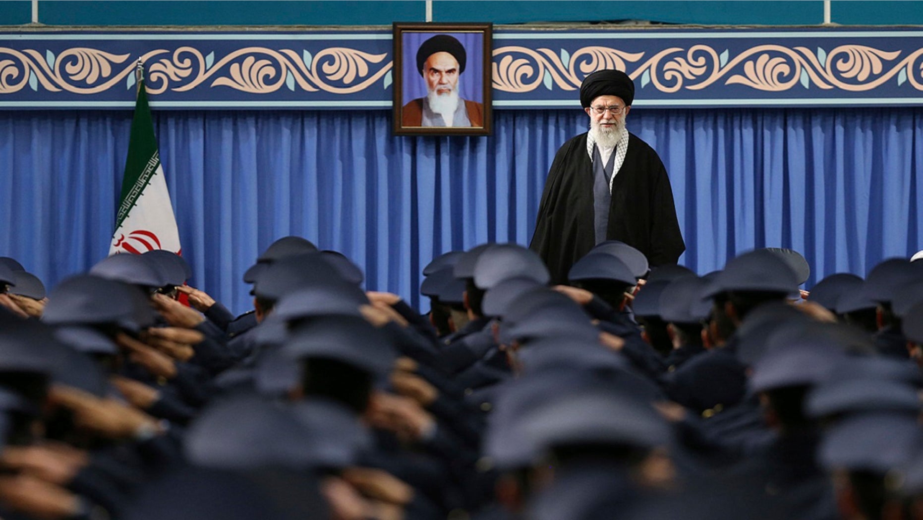 Supreme Leader Ayatollah Ali Khamenei stands as army air force and air defense salute at the start of their meeting in Tehran, Iran, Feb. 8, 2018. A portrait of the late revolutionary founder Ayatollah Khomeini hangs in the background.
