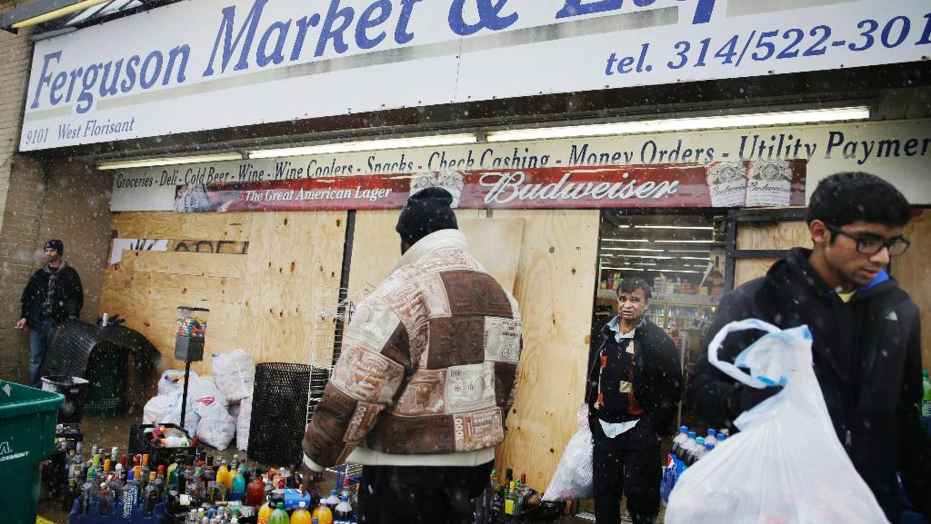 FILE - In this Wednesday, Nov. 26, 2014, file photo, Kush Patel, right, carries out bags of merchandise while helping his uncle Andy Patel, rear, clean up the looting damage from Monday's riots at his store, Ferguson Market and Liquor, in Ferguson, Mo. The store is disputing a new documentary’s claims that surveillance video suggests Michael Brown didn’t rob the store before he was fatally shot by police in Ferguson. One of the filmmakers said he believes the footage shows Brown trading marijuana for a bag of cigarillos early on Aug. 9, 2014, and that Brown intended to come back later for the cigarillos. Store officials said no drug transaction took place and Brown stole the cigarillos while at the store later that day. (AP Photo/David Goldman, File)