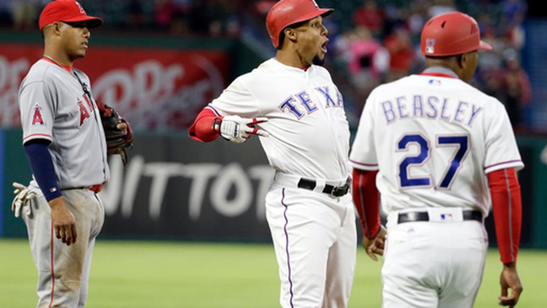 Los Angeles Angels third baseman Yunel Escobar, left, and Texas Rangers third base coach Tony Beasley (27) watch as Rangers' Carlos Gomez, center, celebrates his triple off Angels starter Jesse Chavez during the fifth inning of a baseball game in Arlington, Texas, Saturday, April 29, 2017. (AP Photo/Tony Gutierrez)
