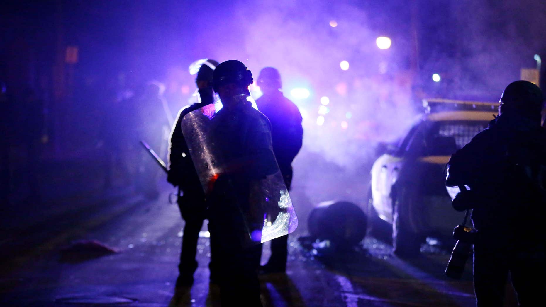 FILE - In this Nov. 25, 2014 file photo, police officers watch protesters as smoke fills the streets in Ferguson, Mo.