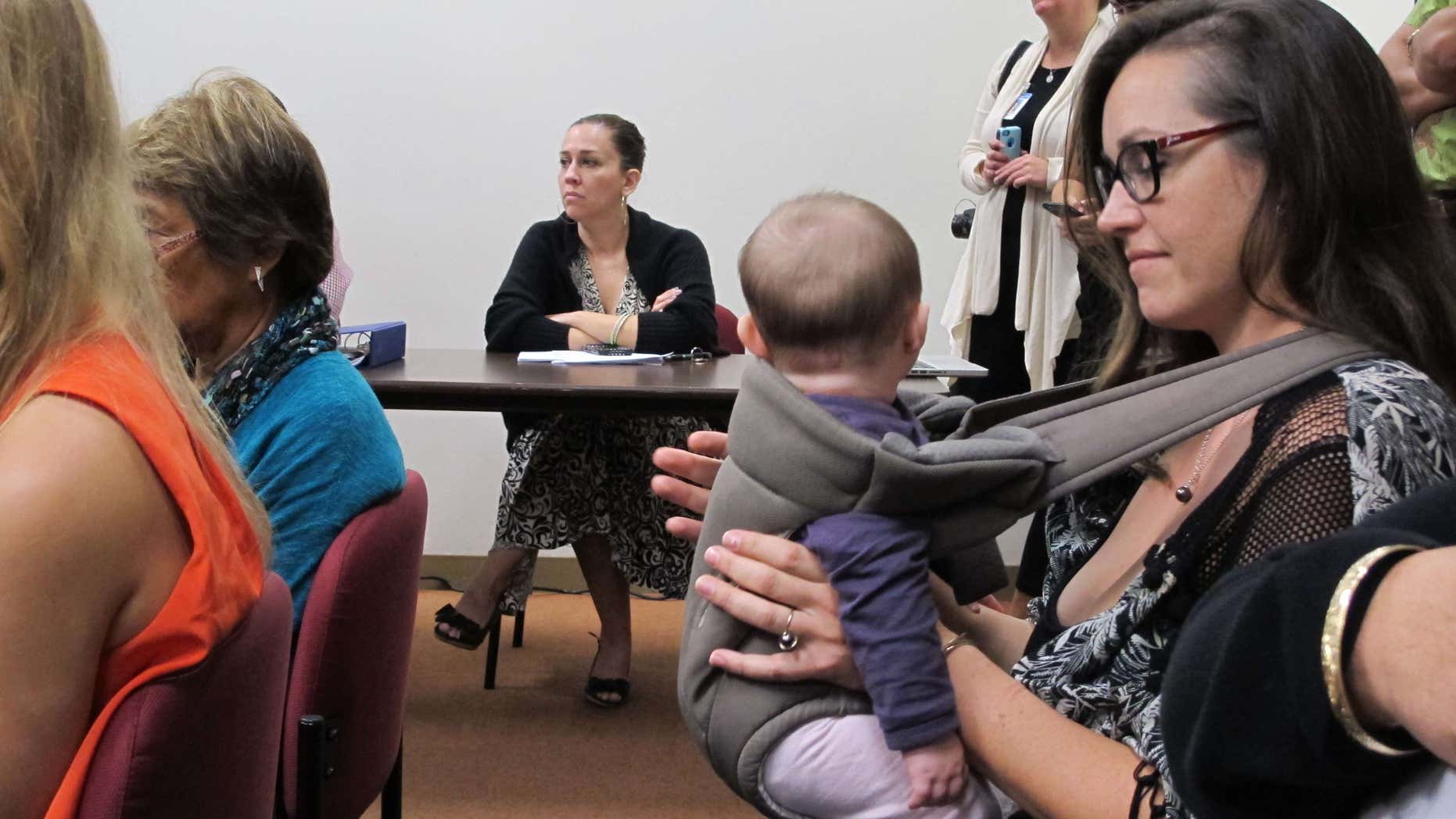 Colleen Chapman, an Oahu resident who's concerned about her children's exposure to pesticide, listens to testimony while holding her daughter at a legislative hearing on Tuesday, Feb. 9, 2016 in Honolulu.