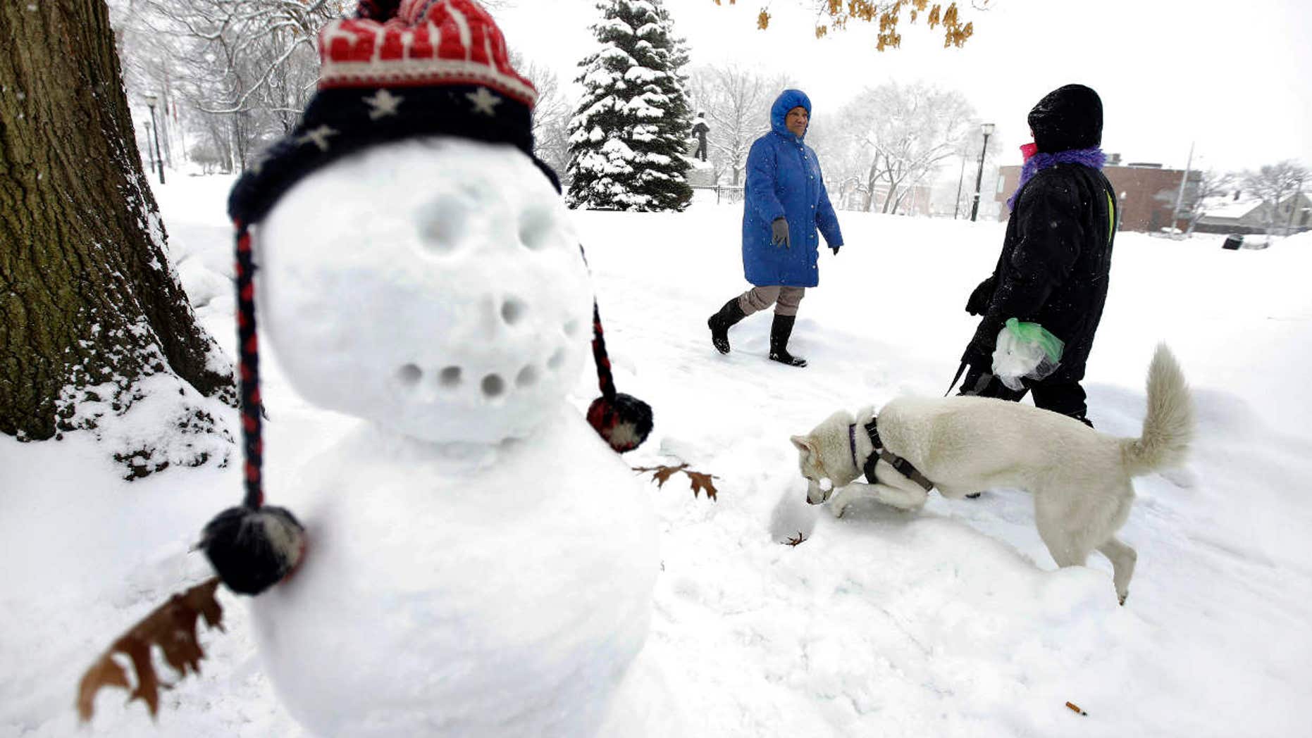 Tina Fuller, 60, of Waltham, Mass., behind center, walks past a snowman and a person walking a dog, Sunday, Feb. 12, 2017, in Waltham, Mass.