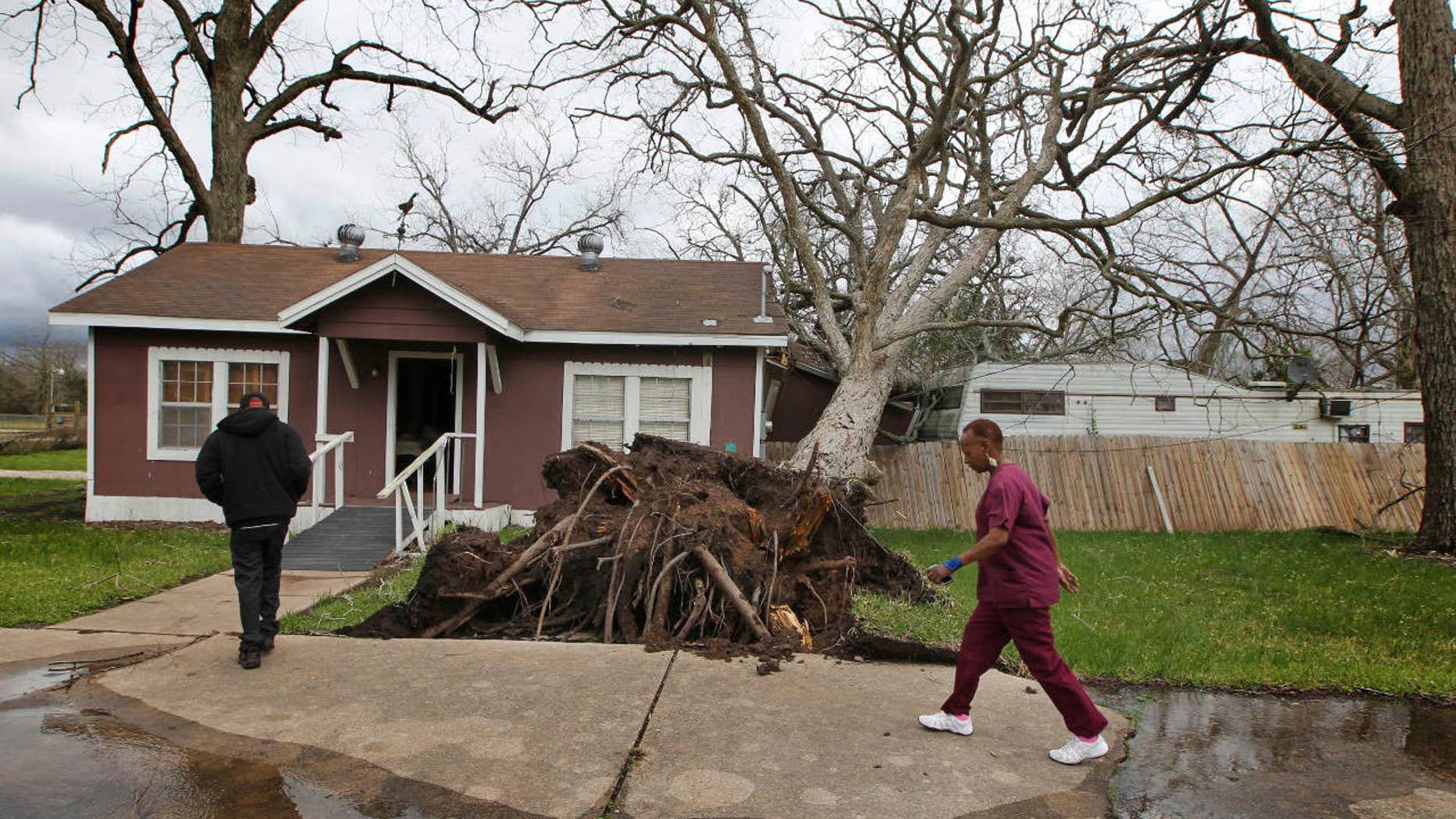 Cheryl Bradshaw, right, and her son Jerard walk past a toppled tree that separated her bathroom from her home Tuesday, Feb. 14, 2017 in Wharton, Texas.