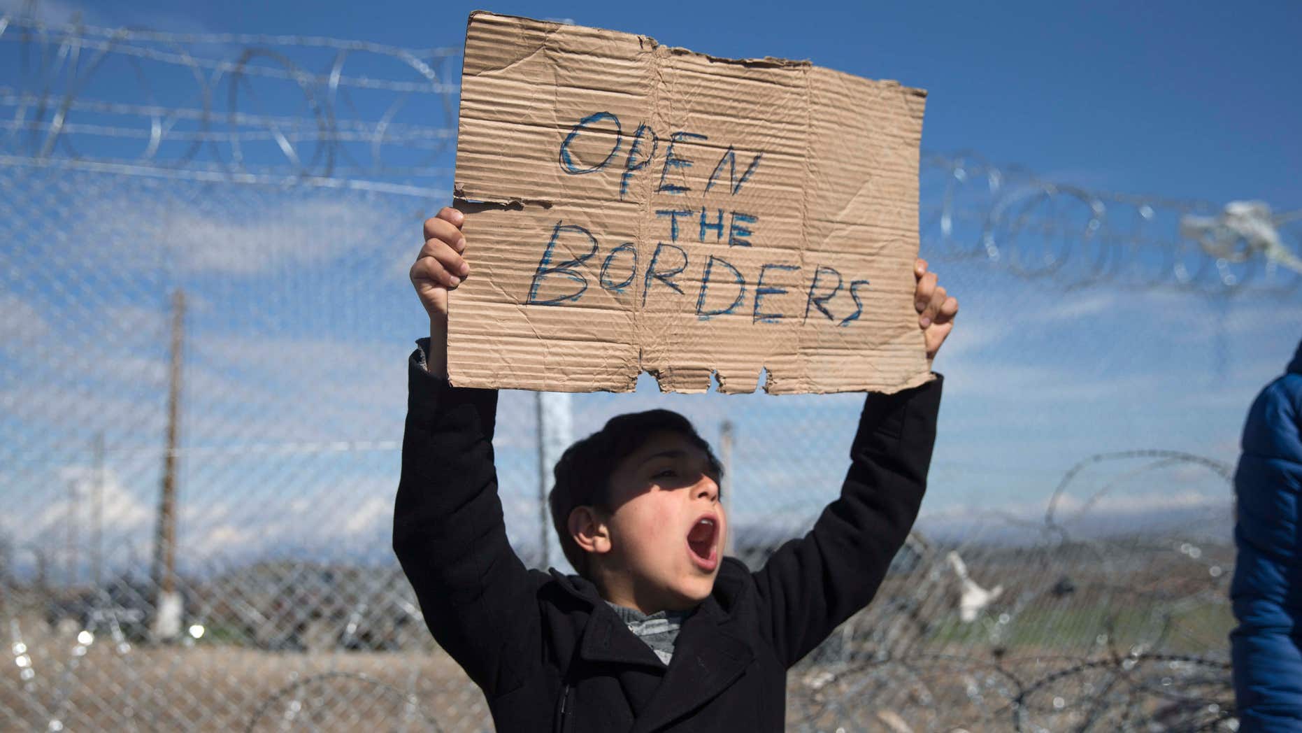Feb. 27, 2016: A boy shouts slogans as he holds a placard during a protest by refugees and migrants in front of the wire fence that separates the Greek side from the Macedonian one at the northern Greek border station of Idomeni.