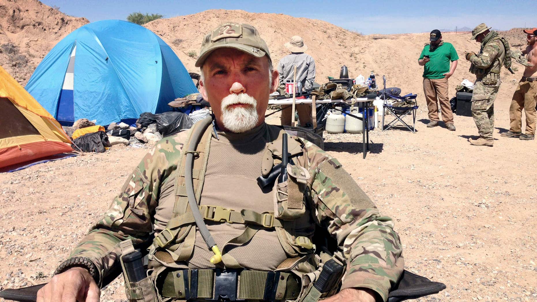 FILE - In this April 16, 2014 file photo, Jerry DeLemus, of Rochester, N.H., sits with a group of self-described militia members camping on rancher Cliven Bundy’s ranch near Bunkerville, Nev.
