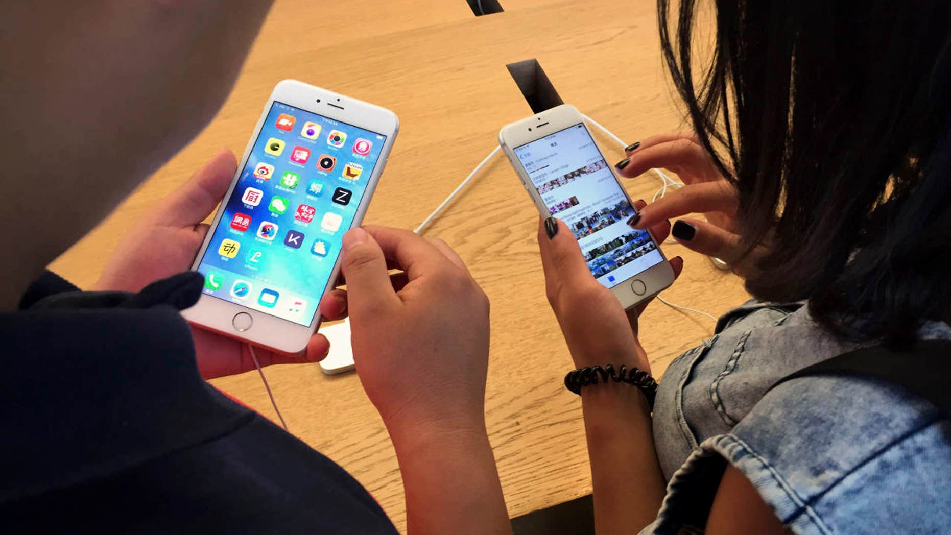 FILE - In this Saturday, June 18, 2016, file photo, customers try out Apple iPhone 6s models on display at an Apple Store in Beijing.