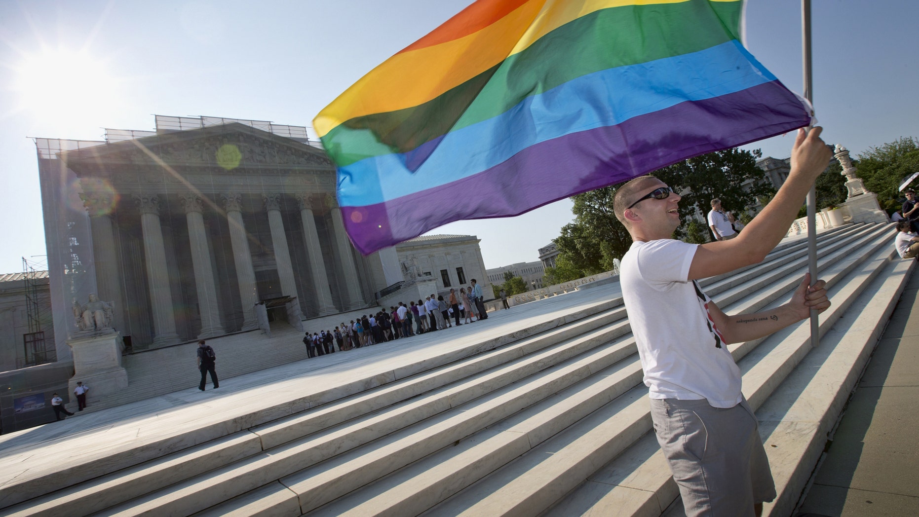 FILE - In this June 25, 2013 file photo, Vin Testa of Washington waves a rainbow flag in support of gay rights outside the Supreme Court in Washington. The Supreme Court will hear arguments over same-sex marriage on April 28 and make audio of the proceedings available later that day. The gay marriage cases mark the only time this term that the court has agreed to the quick release of audio recordings. But the court is continuing its ban on providing video of its sessions or even live-streamed audio. (AP Photo/J. Scott Applewhite, File)