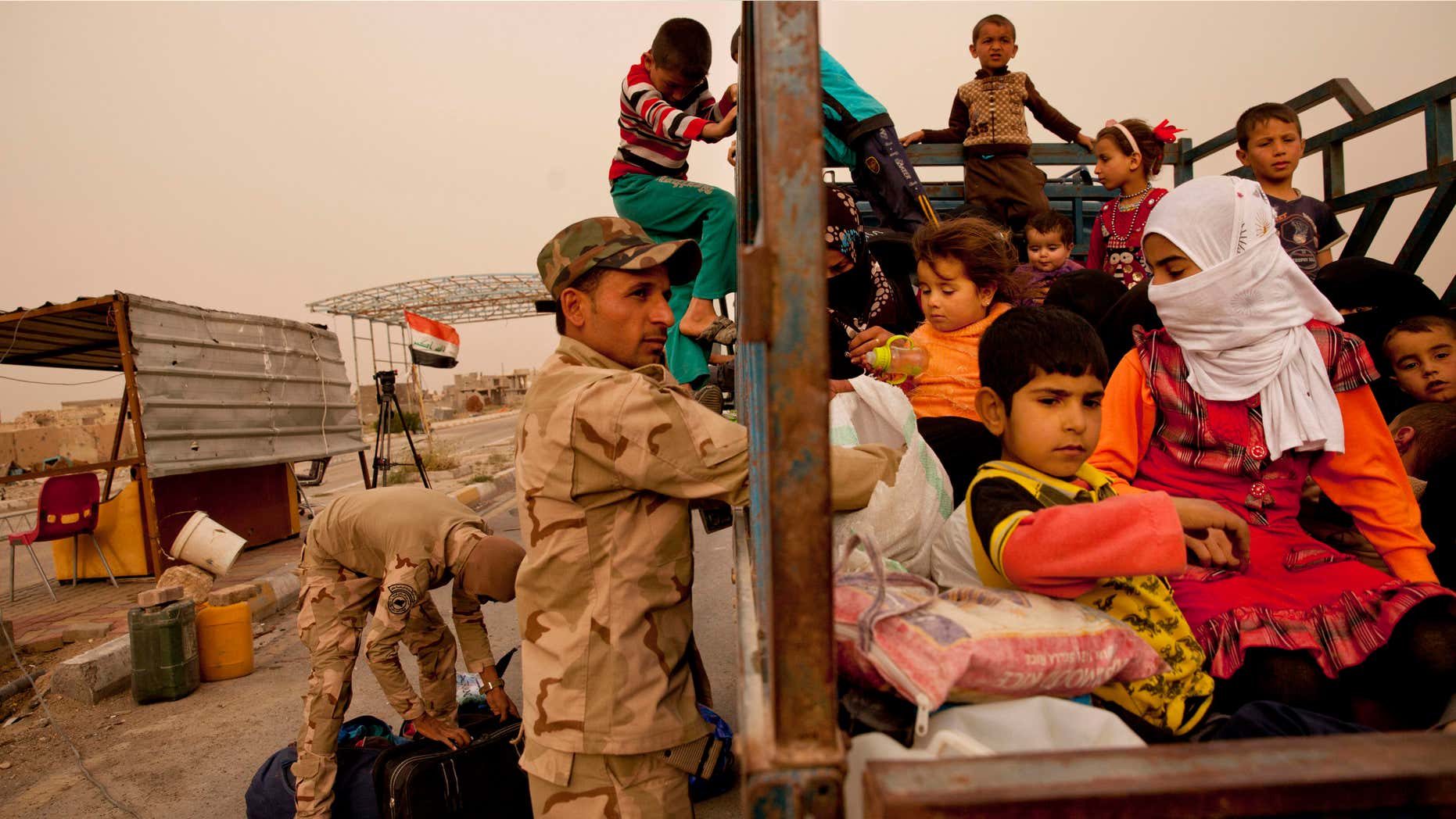 In this Sunday, March 20, 2016 photo, Iraq soldiers search a convoy of families fleeing Islamic State-held Hit, Iraq, at a checkpoint on the western edge of Ramadi, Iraq.