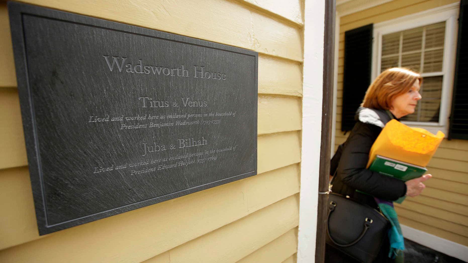 A passer-by walks near a newly unveiled plaque attached to Wadsworth House, Wednesday, April 6, 2016, on the campus of Harvard University that honors four slaves that had been owned by and worked for Harvard's past presidents, in Cambridge, Mass.