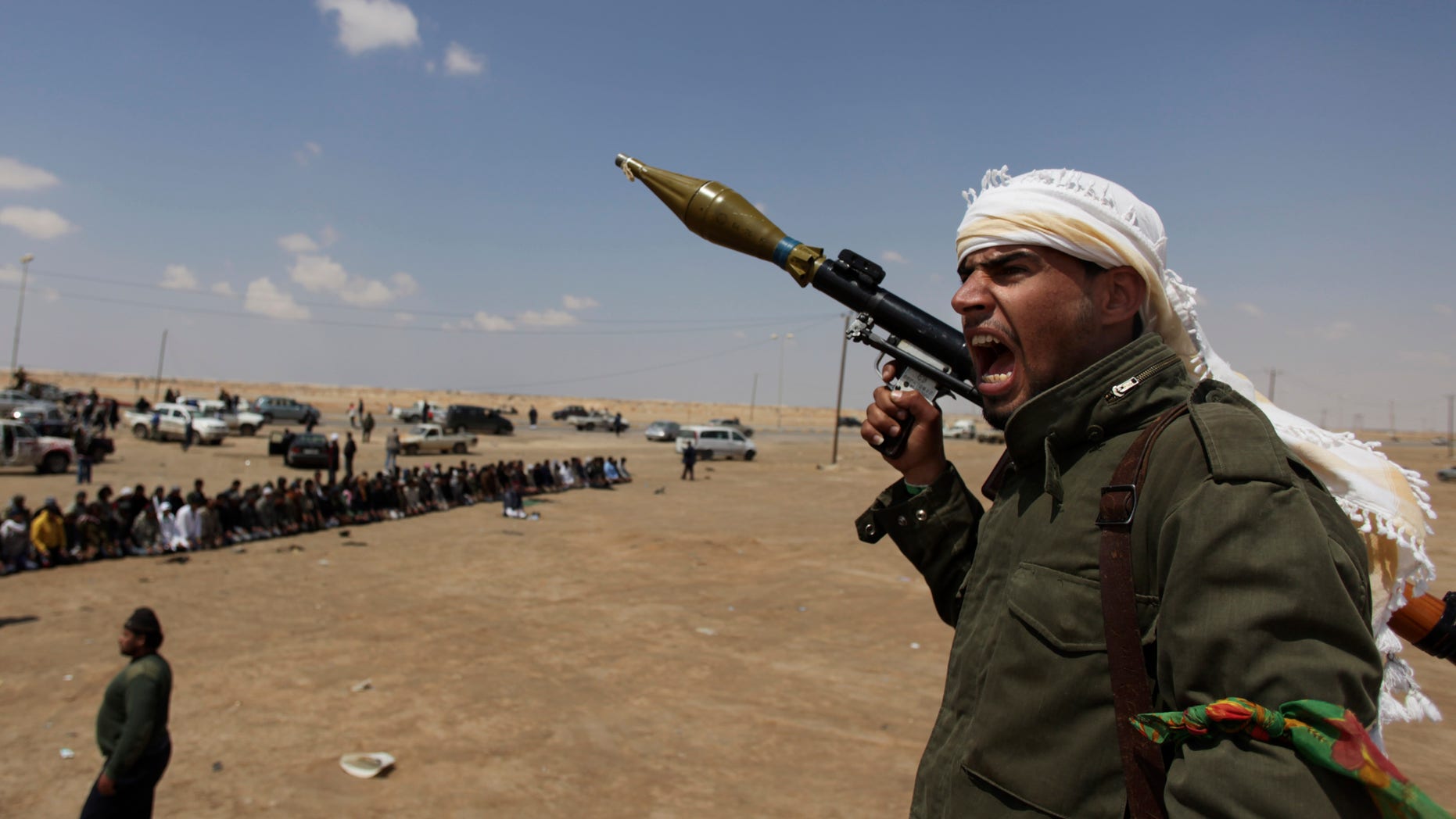 April 8: A Libyan rebel fighter, holding a rocket launcher, shouts religious slogans after gun shots were heard as fellow comrades offer prayers in the background in Ajdabia, Libya.