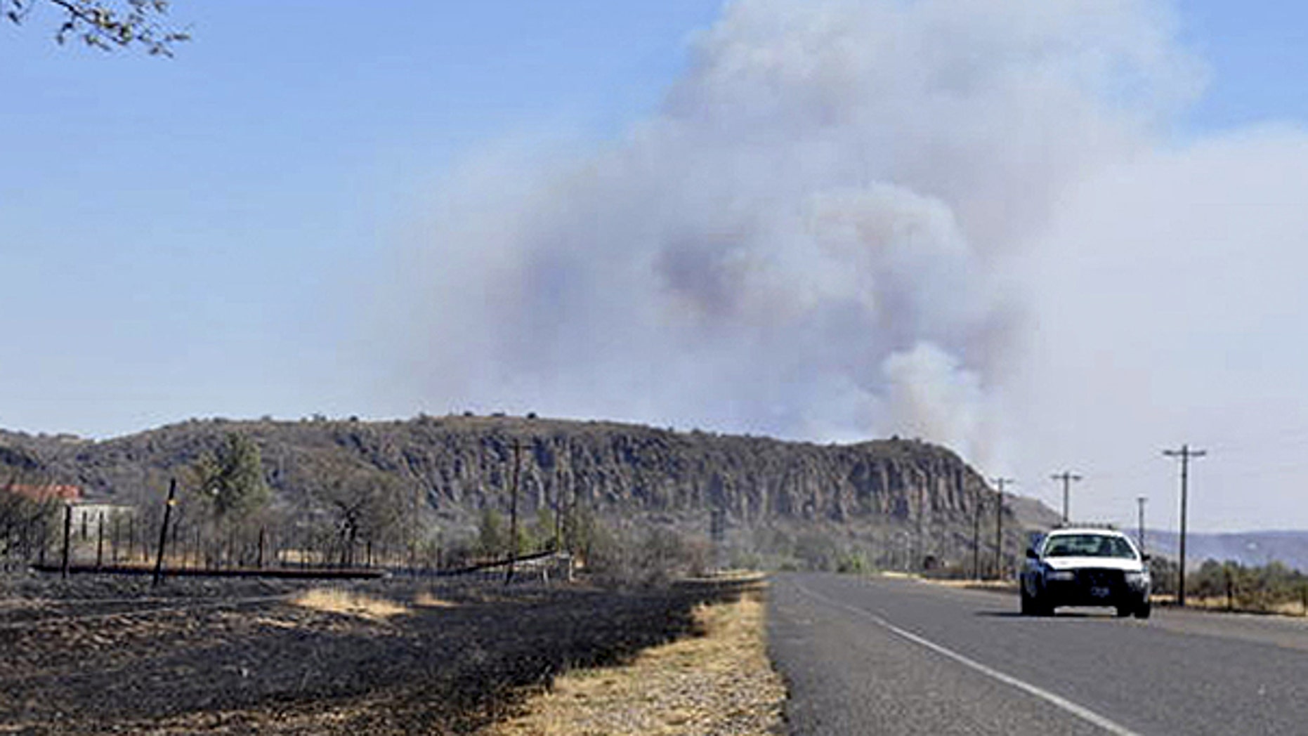 April 10: With smoke rising from a wildfire in the background, a state trooper drives along a road in Fort Davis, Texas.