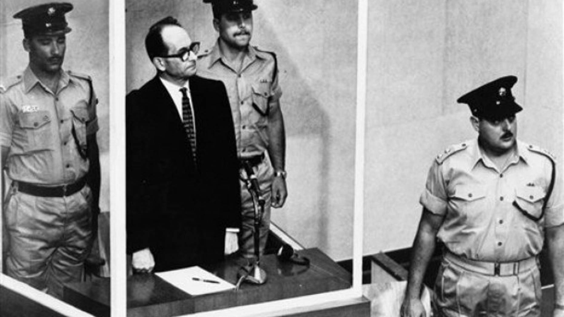 1962: Adolf Eichmann stands in his glass cage, flanked by guards, in the Jerusalem courtroom where he was tried for war crimes committed during World War II. The basics of Adolf Eichmann's story are well-documented. He was commonly known as the "architect of the Holocaust" for his role in coordinating the Nazis' policy of genocide. He fled Germany only to be captured in Argentina by the Mossad, taken to Israel for trial, and hanged.