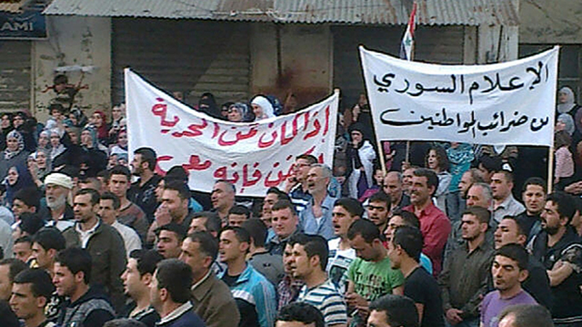 April 17: In this citizen journalism image made on a mobile phone and acquired by the AP, Syrian anti-government protesters hold Arabic banners that read: 'Syrian media from the taxes of the citizens,' right, and 'If the price of freedom is a shroud, it is with me,' as they march during a demonstration in Banias, Syria.