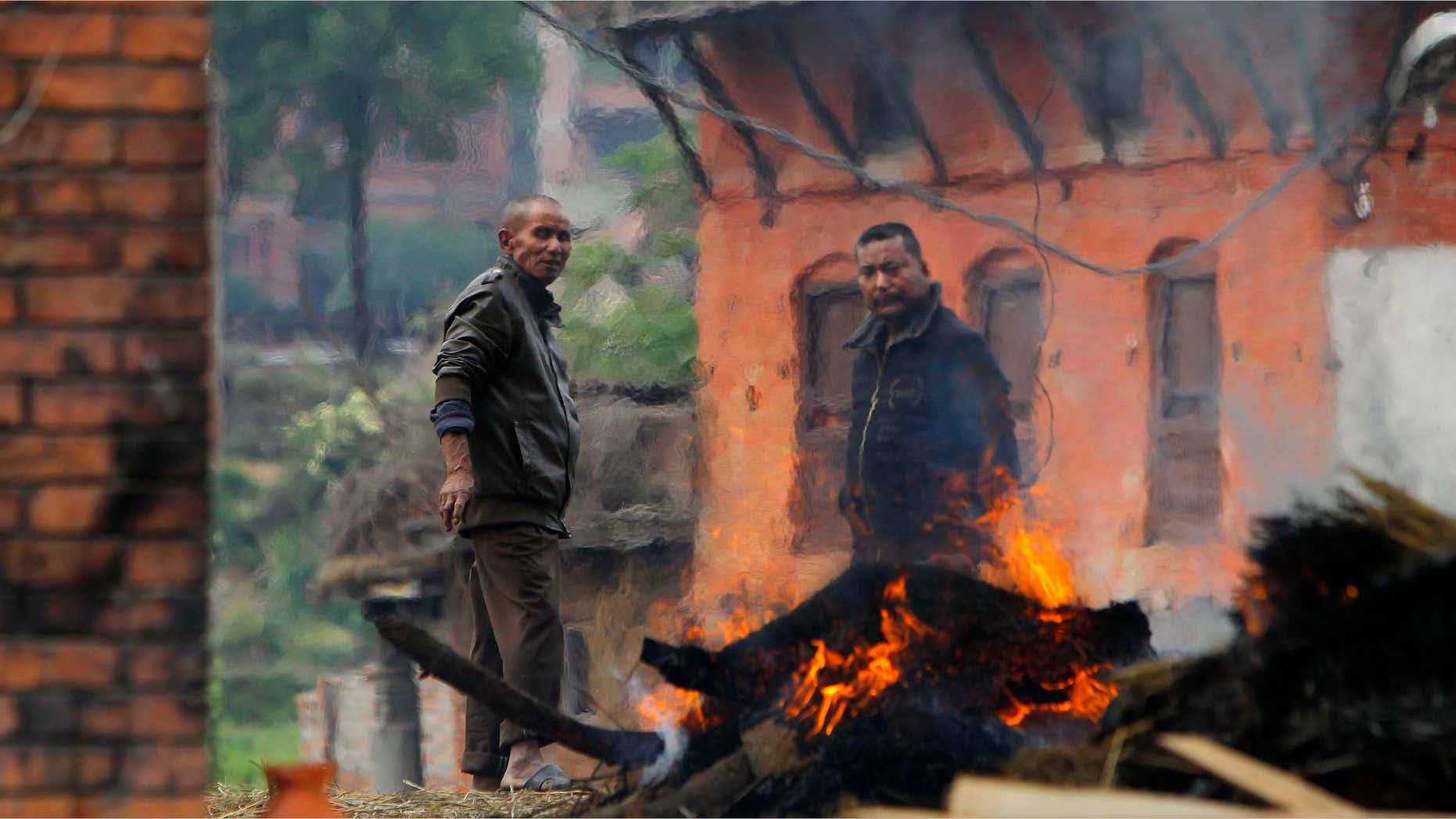 April 26, 2015: Nepalese people stand beside the funeral pyre of a family member who died in Saturday's earthquake in Bhaktapur, Nepal.
