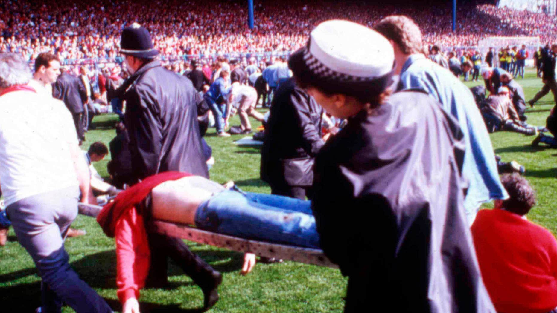 FILE - In this April 15, 1989 file photo police, stewards and supporters tend and care for wounded supporters on the field at Hillsborough Stadium, in Sheffield, England.