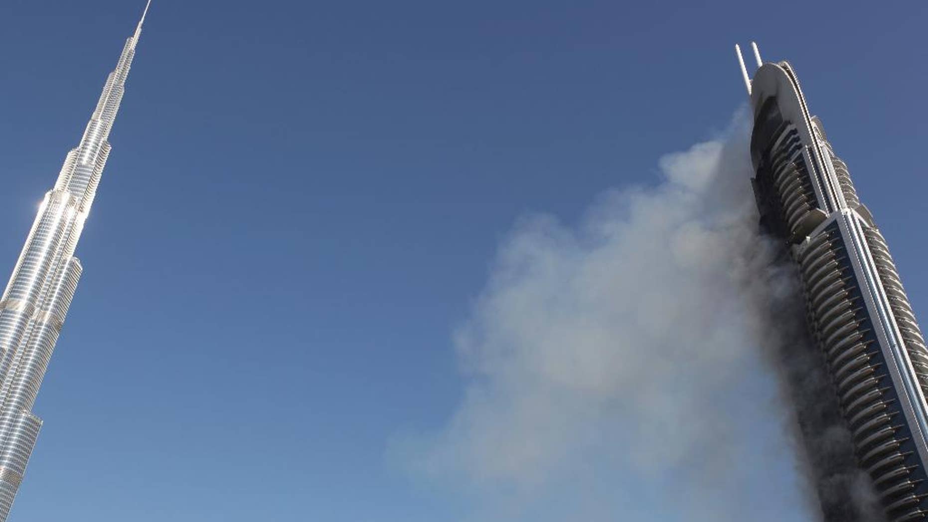 FILE - In this Jan. 1, 2016 file photo, smoke billows from the 63-story The Address Downtown skyscraper near the Burj Khalifa, the world's tallest building, in Dubai, United Arab Emirates. The developer of the world's tallest building says it will collect $332.4 million from its insurer to cover damage sustained during a dramatic New Year's Eve fire at one of its Dubai hotels. Emaar Properties said in a filing to the Dubai Financial Market that it has agreed with Orient Insurance to recover the 1.22 billion dirham claim related to the Dec. 31, 2015 blaze. (AP Photo/Jon Gambrell, File)