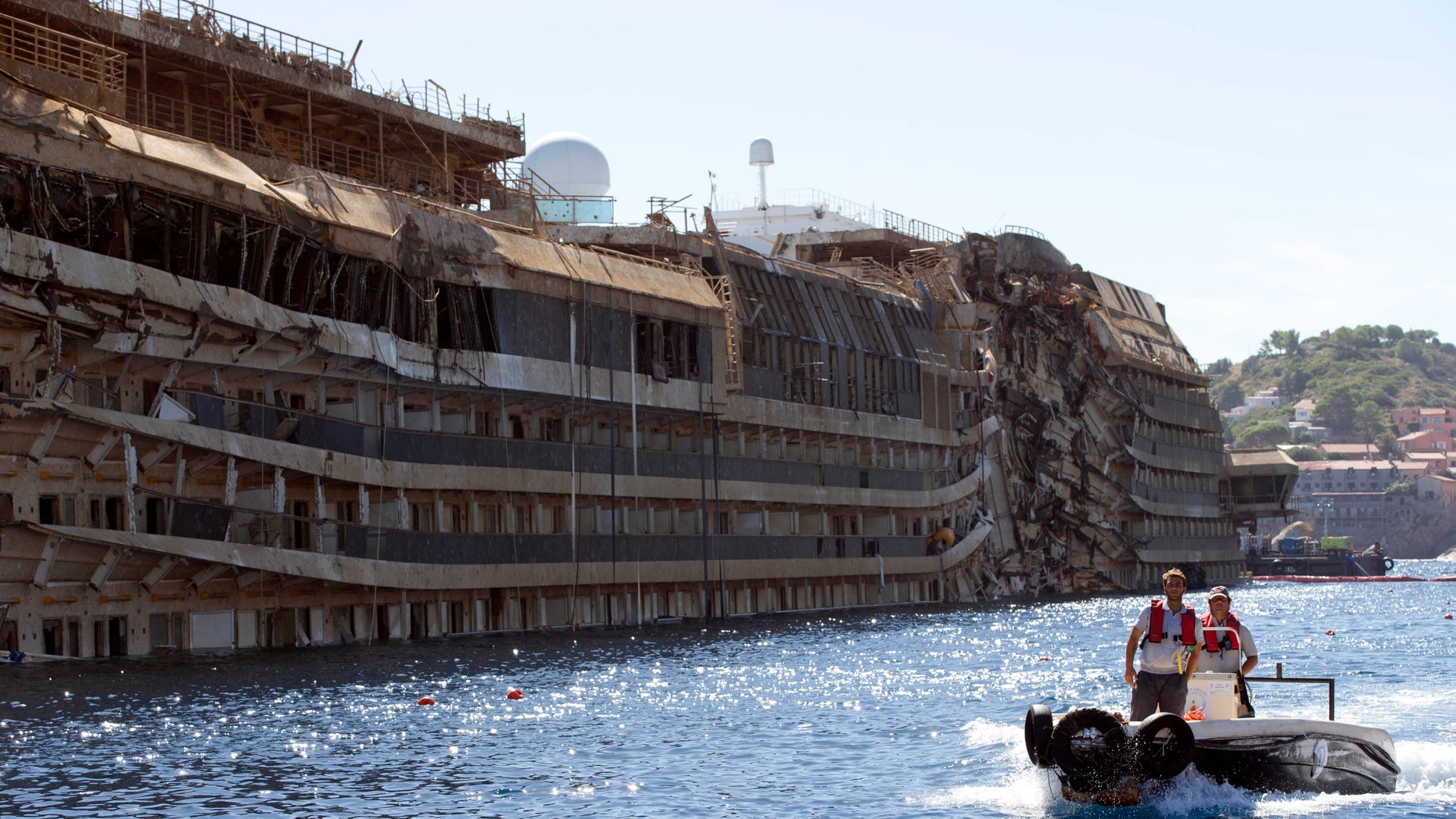 FILE - In this Sept. 18, 2013 file photo, a small boat navigates past the damaged side of the Costa Concordia ship after it was pulled upright, on the Tuscan Island of Giglio, Italy. Divers searching the submerged part of the wreck of the cruise ship have found the remains of one of the two people still missing from the 2012 disaster. Officials believe the remains belong to Russel Rebello, an Indian waiter. Thirty-two people died when the Concordia slammed into a reef off the Tuscan island of Giglio and capsized on Jan. 13, 2012. (AP Photo/Andrew Medichini, file)