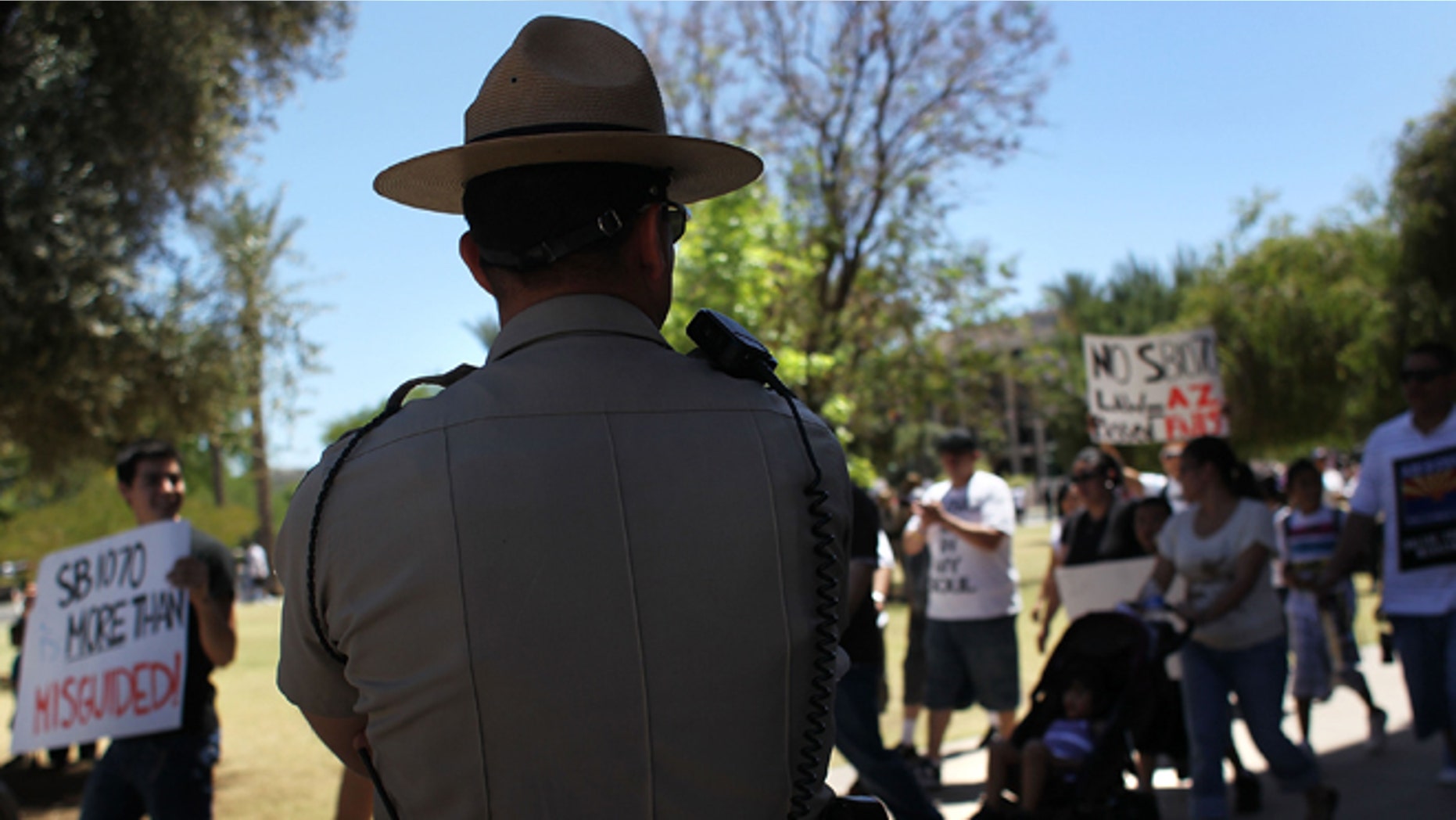 PHOENIX - MAY 01: A police officer watches demonstrators protest Arizona's new immigration enforcement law during a May Day rally at the state capitol building on May 1, 2010 in Phoenix, Arizona. Thousands of people in cities across the United States protested the immigration law, which critics have said could encourage racial profiling against Hispanics by police officers. (Photo by John Moore/Getty Images)