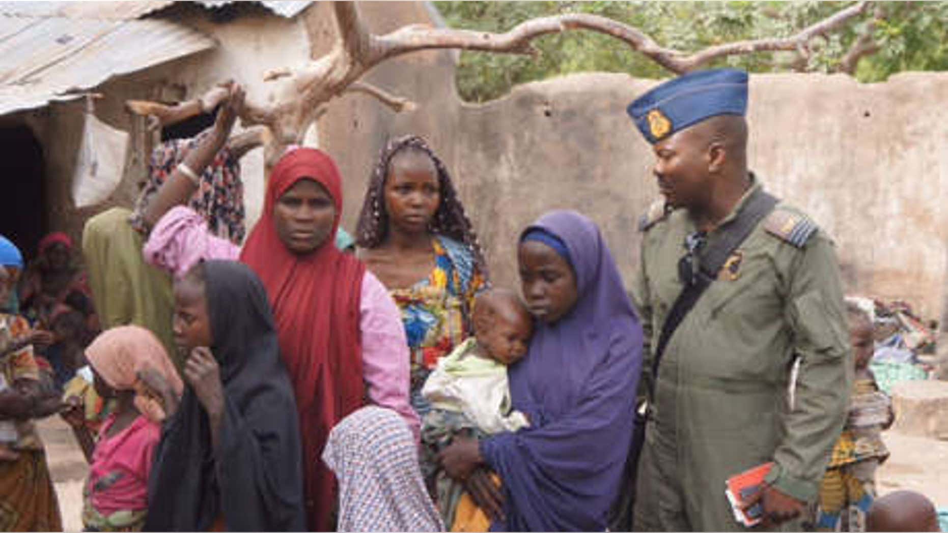 April 29, 2015: A Nigerian soldier stands next to woman and children that were allegedly rescued by the Nigerian Military after being taken by Islamic extremists in Sambisa Forest, Nigeria.