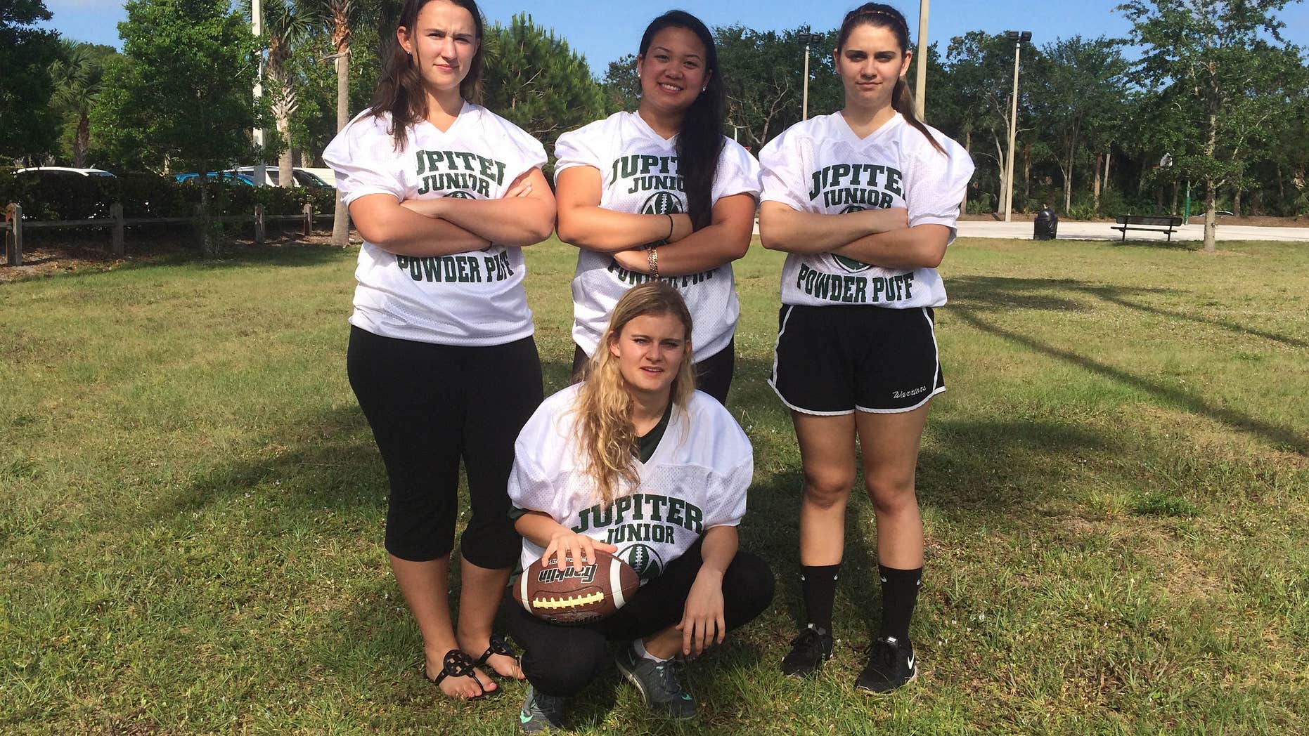 In this photo taken Monday, May 2, 2016, Jupiter High powderpuff football players Caitlin Walsh, Megan Mendoza, Haley Osborne and Savannah Tardonia, in front with ball, pose for a group photo in Jupiter, Fla.