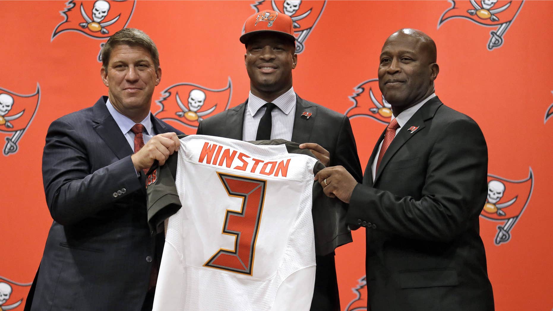 May 1, 2015: Tampa Bay Buccaneers first-round draft pick Jameis Winston, center, holds his jersey as he stands with general manager Jason Licht, left, and head coach Lovie Smith, right, during a news conference.