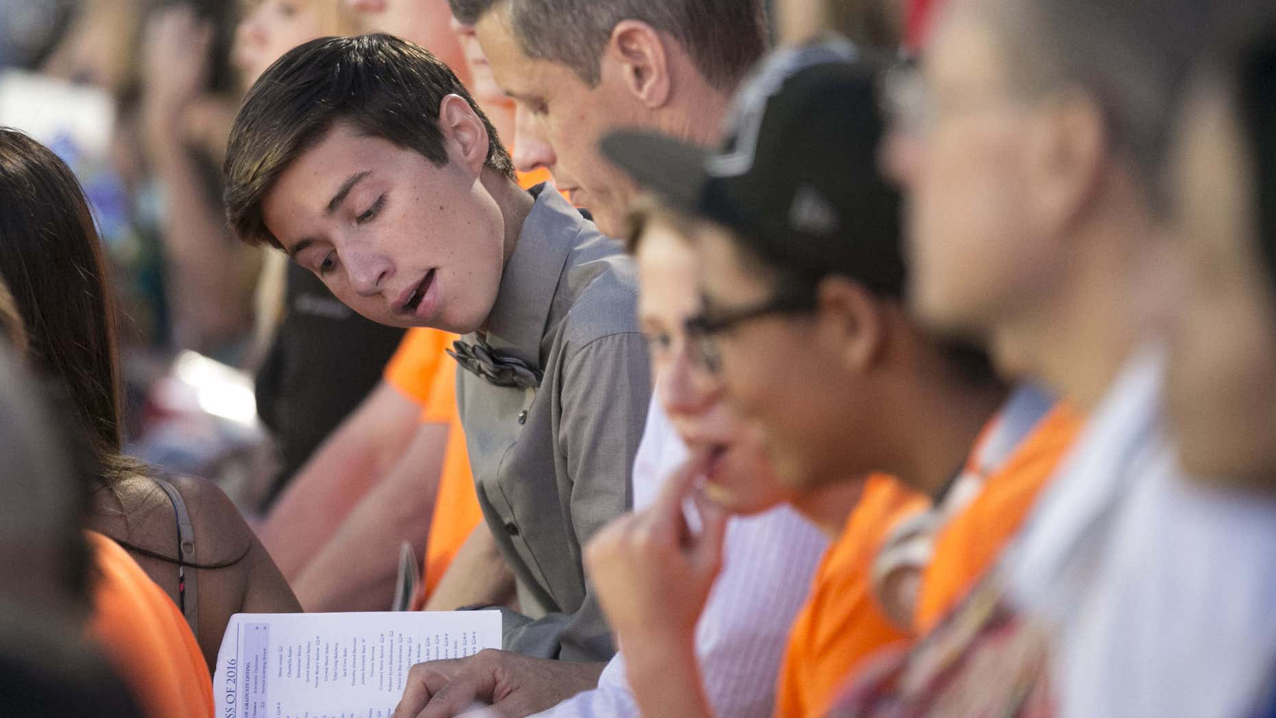 In this photo taken, Thursday evening, May 26, 2016, Stephen Dwyer, student body president and member of the Class of 2016 of Dobson High School, looks at the graduation program while sitting in the bleachers during the Dobson High School graduation in Mesa, Ariz.