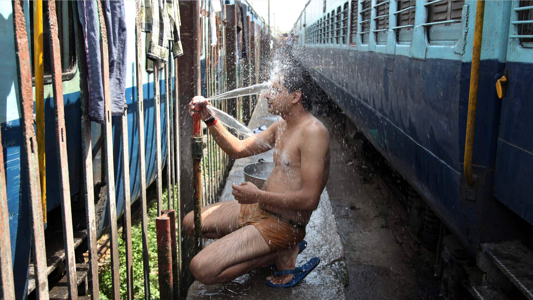 May 25, 2015: An Indian passenger takes a bath beside rail tracks on a hot summer day at a railway station in Jammu, India.