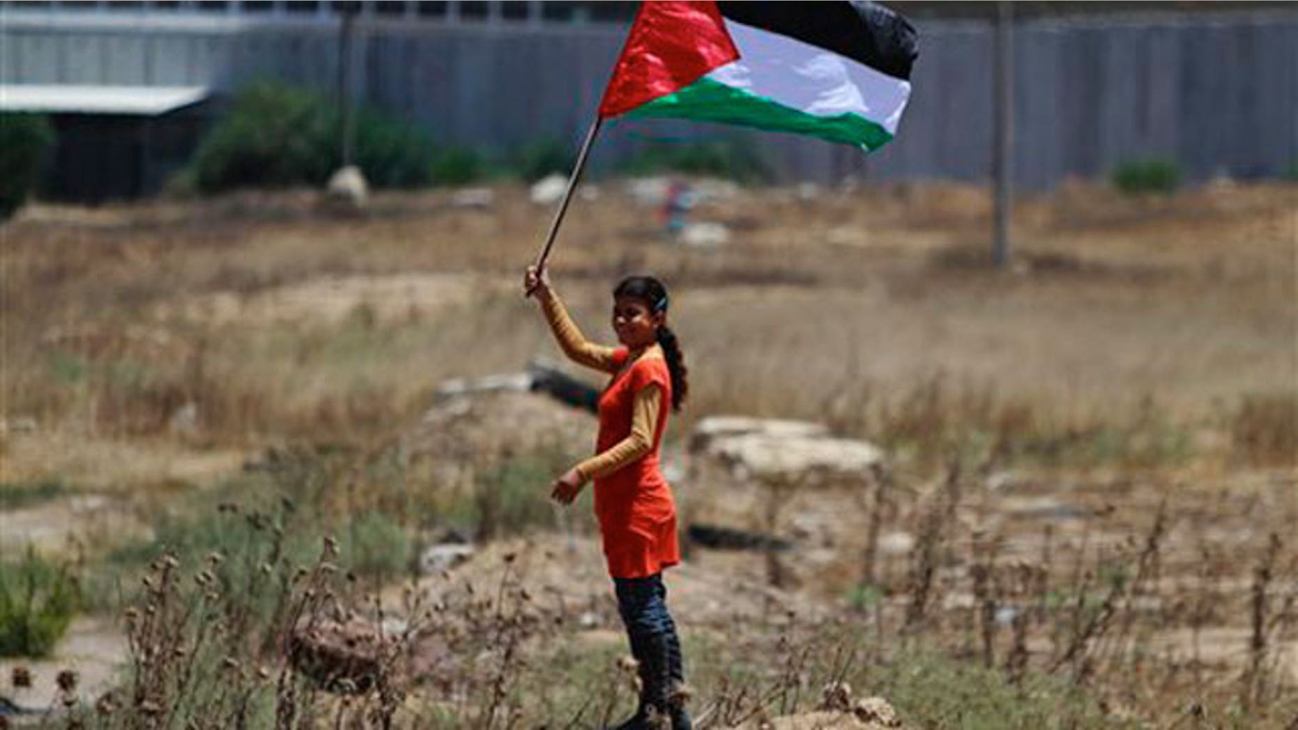 June 8: A Palestinian girl holding a national flag stands near the border line with Israel, background, during a weekly protest march against Israel, in Beit Hanoun, northern Gaza Strip.