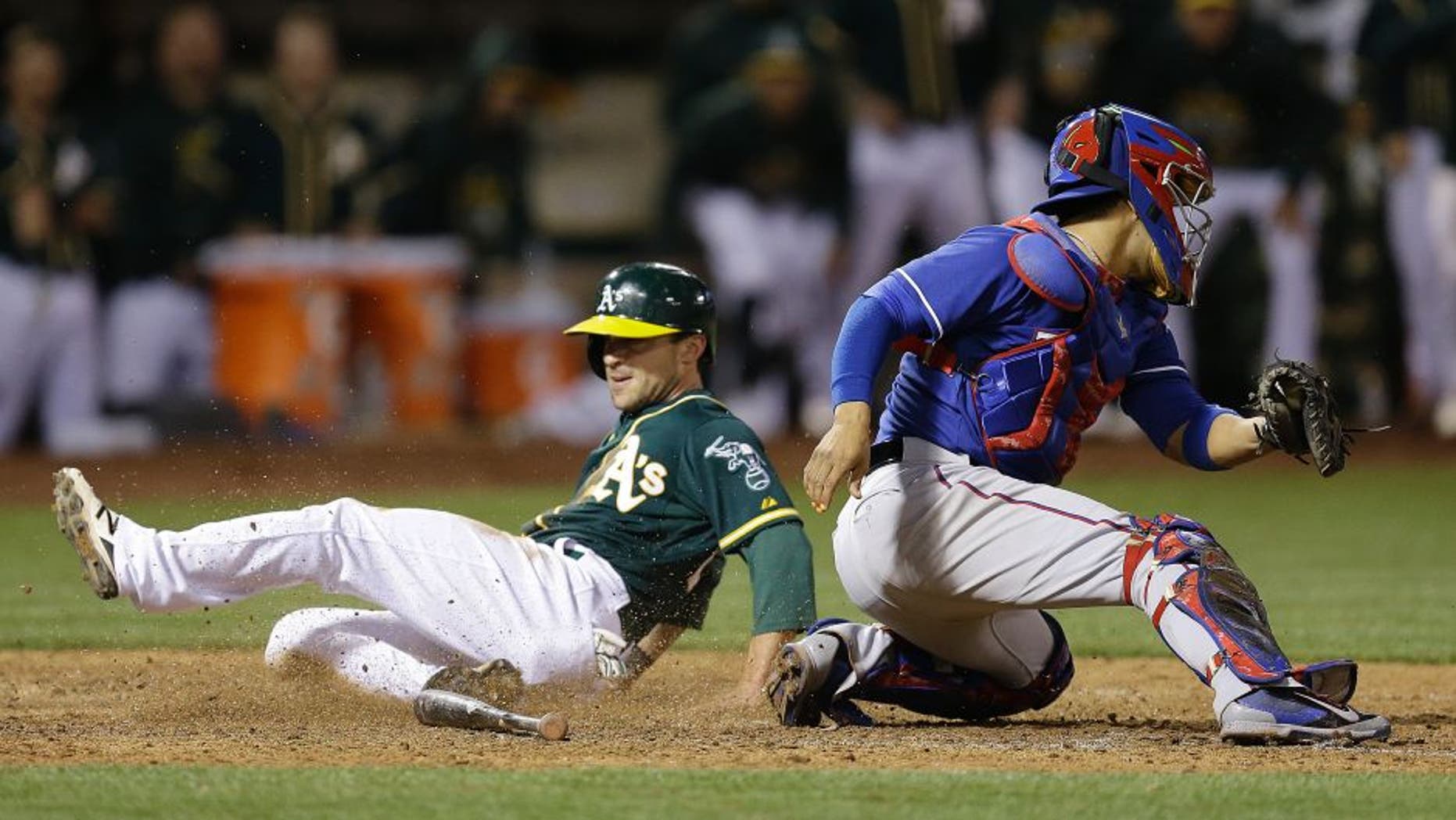 Oakland Athletics' Sam Fuld, left, slides to score behind Texas Rangers catcher Robinson Chirinos in the ninth inning of a baseball game Wednesday, June 10, 2015, in Oakland, Calif. The A's scored the winning run on the play, on a single by Josh Reddick. (AP Photo/Ben Margot)