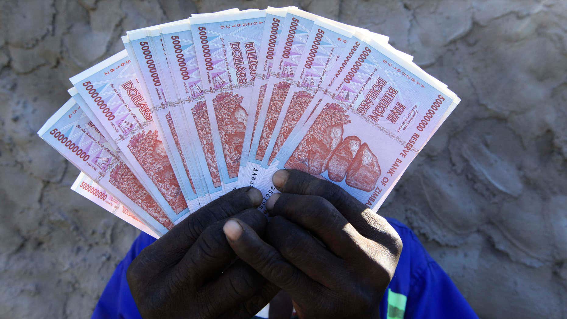 June 12, 2015: A man holds a handful of 5 Billion Zimbabwean dollar notes, in Harare.