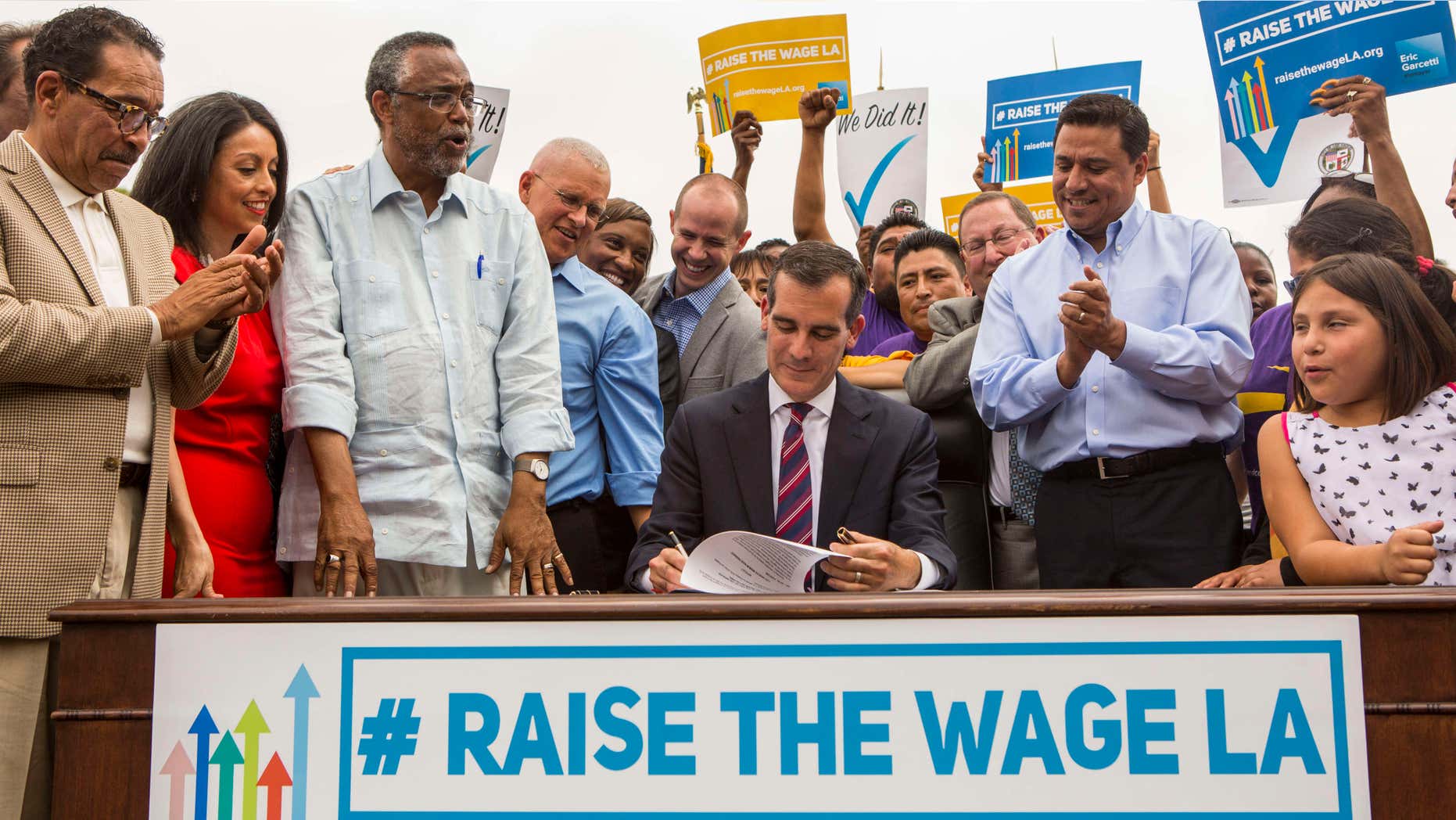June 13, 2015: Los Angeles Mayor Eric Garcetti, center, joins members of the City Council and community leaders as he signs into law an ordinance that will gradually raise the minimum wage to $15 an hour by 2020, in at Martin Luther King Jr. Park in Los Angeles.