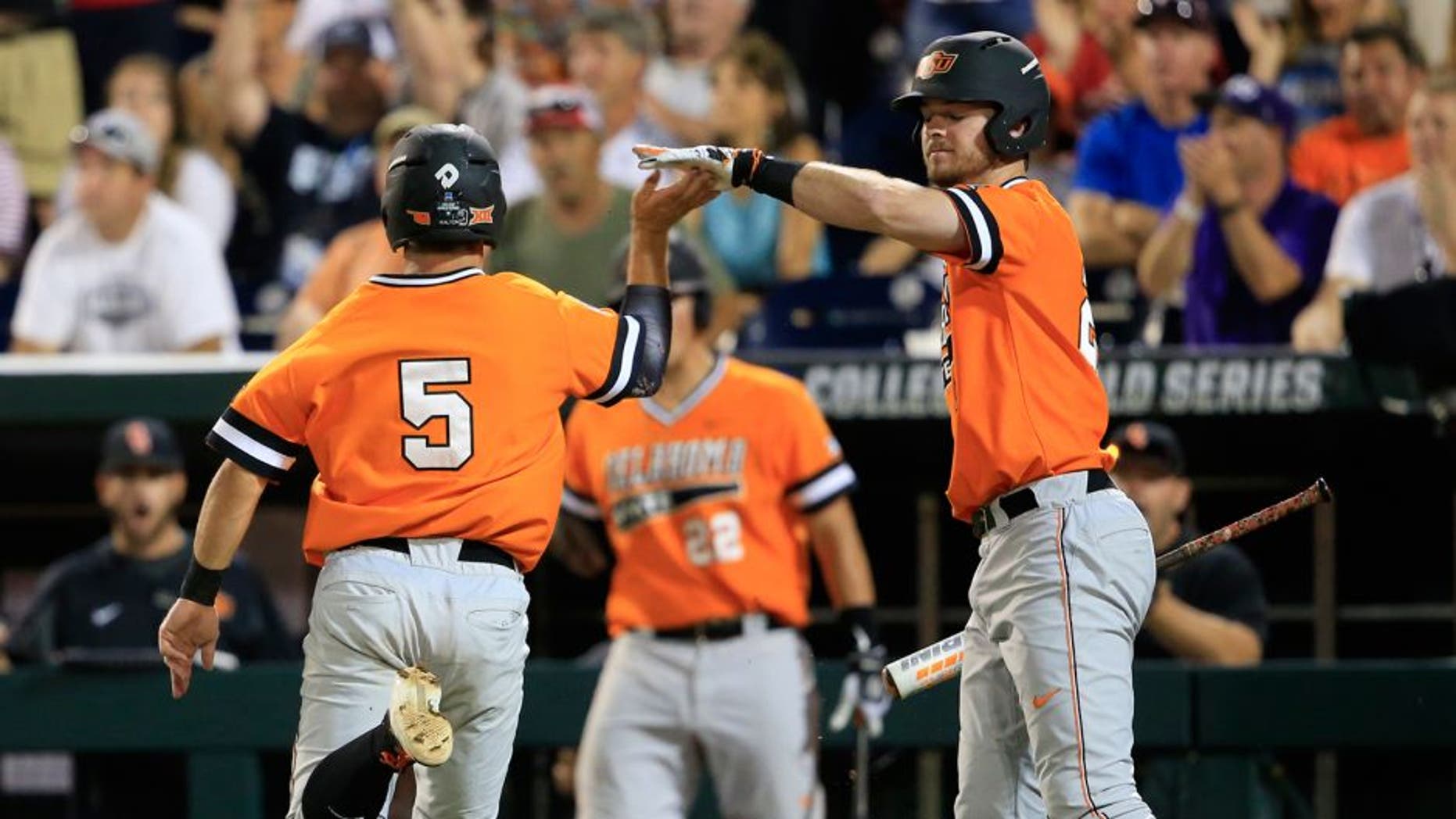 Oklahoma State's Donnie Walton, left, is congratulated by Conor Costello after scoring on a single by Garrett Benge during the fourth inning of an NCAA College World Series baseball game against Arizona, Monday, June 20, 2016, in Omaha, Neb. (AP Photo/Nati Harnik)