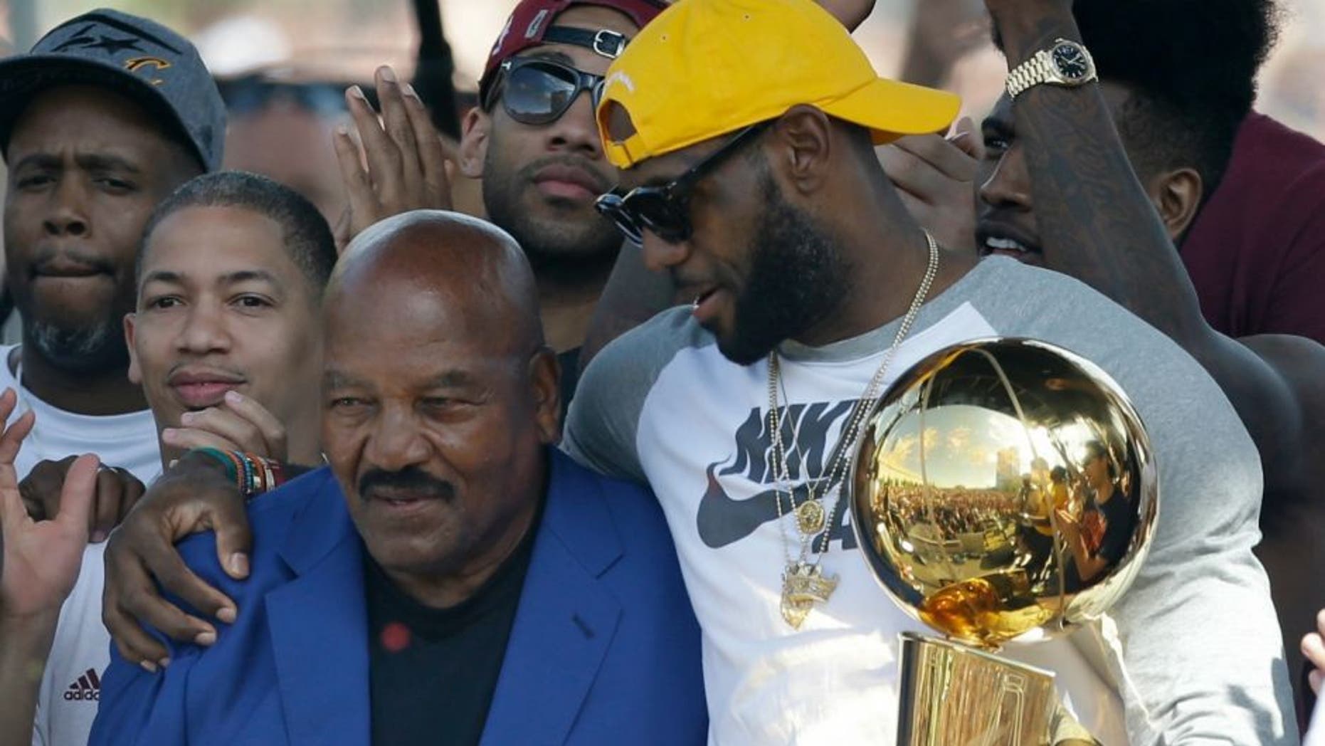 Former Cleveland Brown' Jim Brown, left, passes the Larry O'Brien NBA Championship Trophy to LeBron James during a rally, Wednesday, June 22, 2016, in Cleveland. The Cavaliers made history by overcoming a 3-1 deficit to beat the Golden State Warriors in the NBA Finals and end the city's 52-year drought without a professional sports championship. (AP Photo/Tony Dejak)