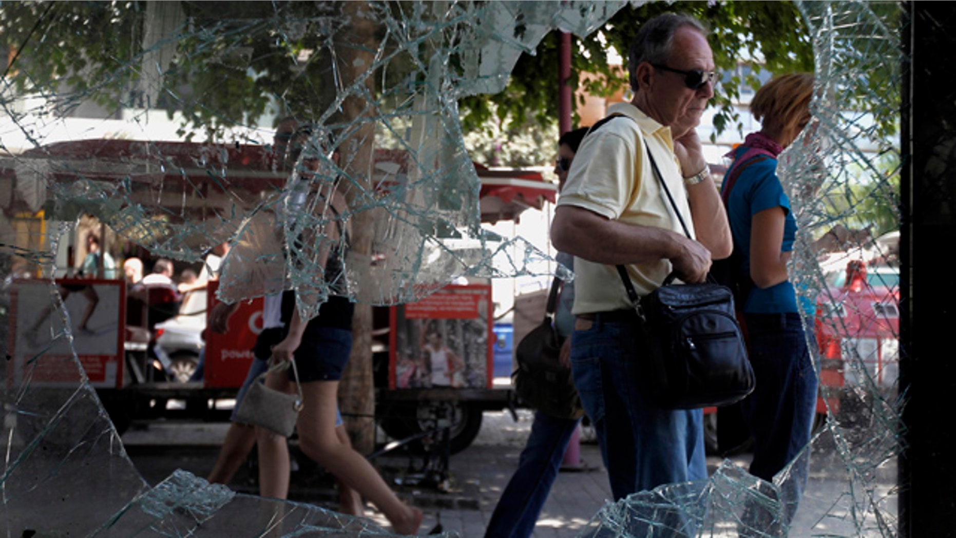 June 30: Athenians walk by a broken window of a building in central Athens.