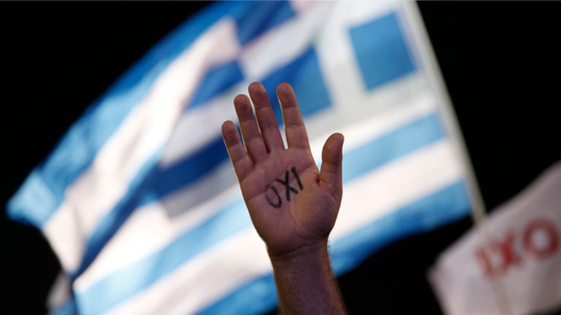 July 3, 2015: A demonstrator rises his hand reading the word ''No'' as a Greek flag waves during a rally organized by supporters of the No vote in Athens.